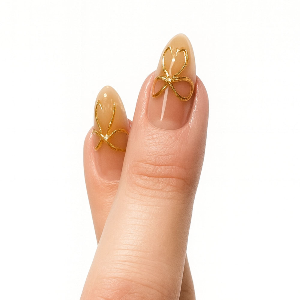 Nude press-on nagels met gouden strikjes in almond vorm, Golden Bow Babe van Freaky Nails.