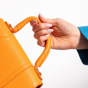 Close-up van Soft Serve short oval nude press on nagels met een oranje handtas - Freaky Nails