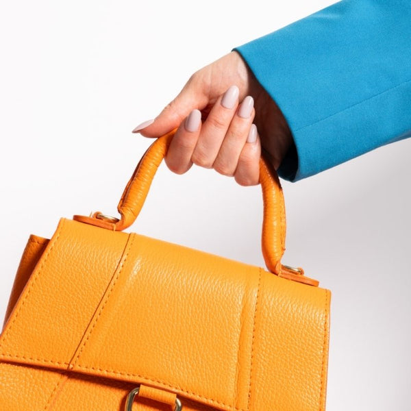 Hand met Soft Serve short oval nude press on nagels die een oranje tas vasthoudt - Freaky Nails