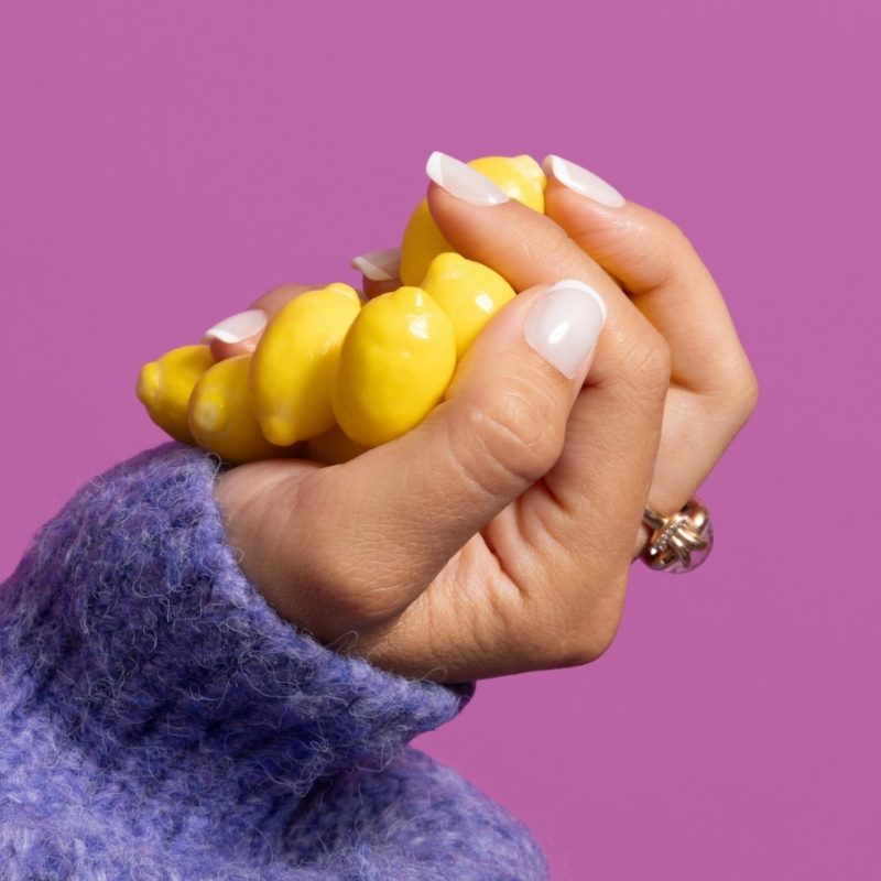 Hand met Too Polished To Care french almond press on nagels en gele accessoire - Freaky Nails